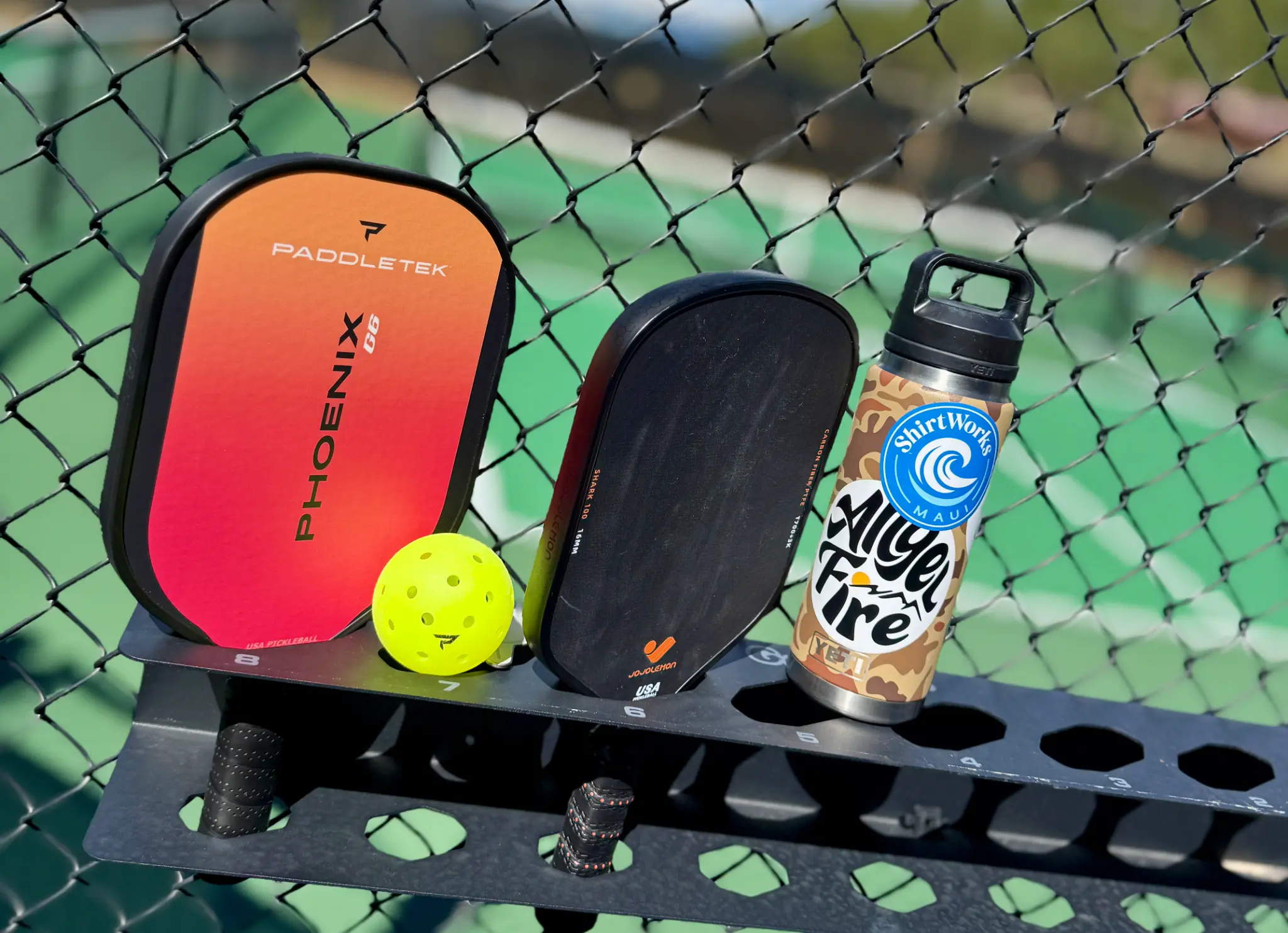 Two pickleball paddles, a bright yellow pickleball, and a water bottle at Angel Fire Resort's Olympic Park Racquet Center